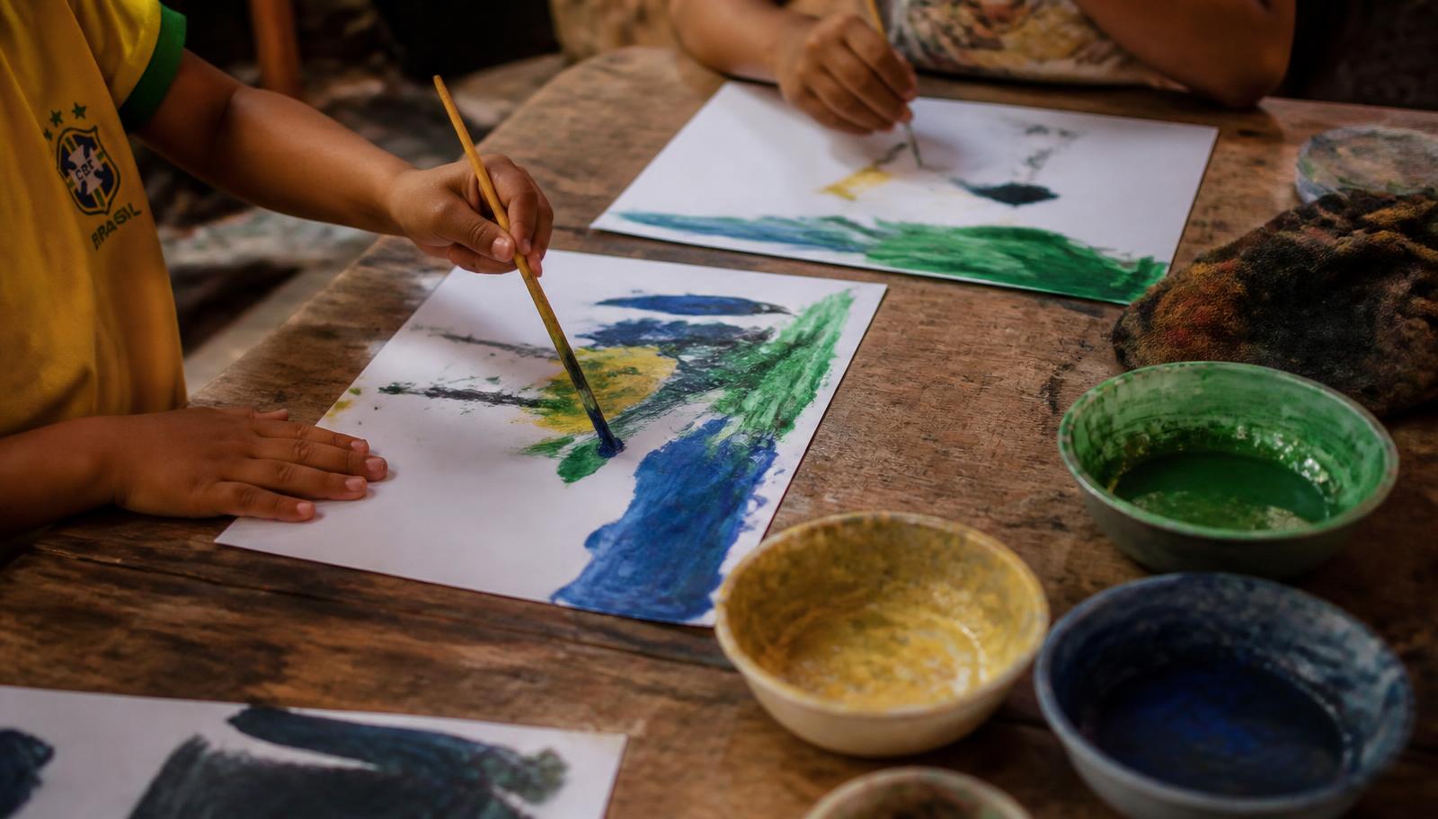 Mãos de crianças pintando com guache sobre uma mesa de madeira em uma creche
